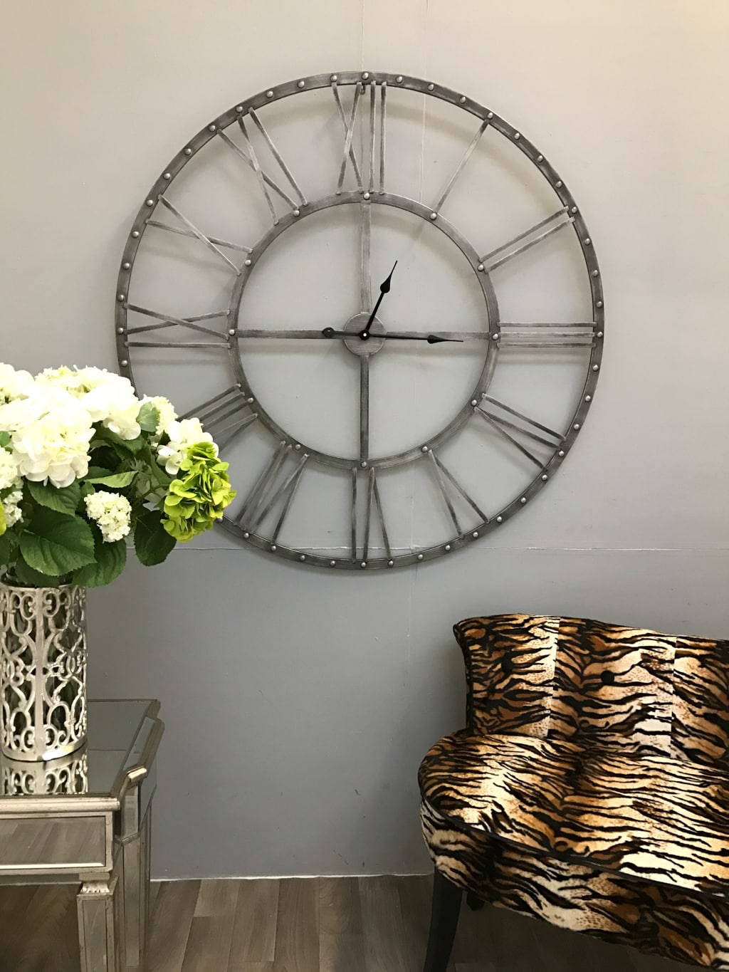 Round Skeleton Wall Clock in Antiqued Silver hanging on a grey wall